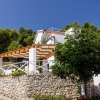 Villa bianca con pergolato di legno e giardino fiorito.