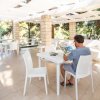 Una terrazza con tavoli bianchi e una persona seduta che legge.