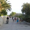 Passeggiata con persone, palme e un muro di pietra a lato del viale.