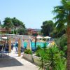 Area con tavoli all'aperto, ombrelloni e palme vicino a una piscina.