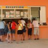 Persone in fila davanti a un banco di reception con cartelli.