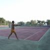 Un uomo gioca a tennis su un campo all'aperto con alberi sullo sfondo.