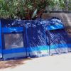 Una tenda blu montata all'ombra di un albero, vicino a un muro di pietra.