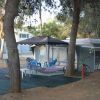 Un campeggio con roulotte, tavolo e sedie blu sotto un gazebo, e un'amaca tra due alberi.