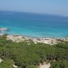 Vista aerea di una spiaggia con mare azzurro e foresta.