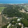 Veduta aerea di campi agricoli e colline con il mare in lontananza.