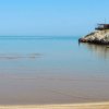 Spiaggia con sabbia e mare calmo, persone giocano in acqua.