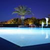 Una piscina illuminata di notte con palme sullo sfondo.