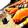 Spiaggia affollata con ombrelloni arancioni e lettini.