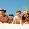 Una famiglia sorridente con maschere da snorkeling sdraiata sulla sabbia.