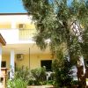 Villa gialla con balcone, circondata da alberi e piante verdi.