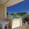 Un balcone con tavolo e sedie bianche, vista su alberi e cielo blu.