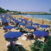 Spiaggia sabbiosa con ombrelloni blu e lettini, mare sullo sfondo.
