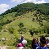 Gruppo di persone su un prato con colline verdi.