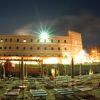 Edificio storico illuminato di notte con sdraio e ombrelloni chiusi in primo piano.